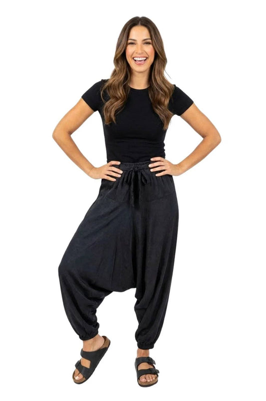 A woman modeling a black short-sleeve top and black harem-style pants with a drawstring waist, paired with black sandals, against a plain white background.