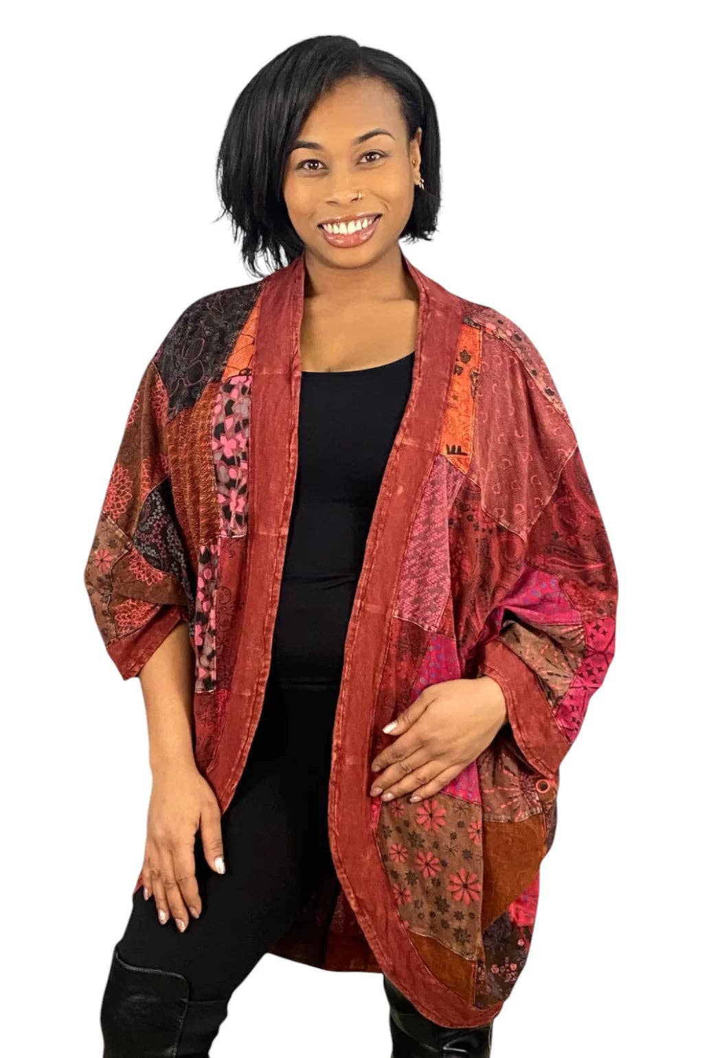 A woman modeling a patchwork kimono jacket with a mix of rust red, pink, orange, and brown patterns, worn over a black top and black pants against a white background.